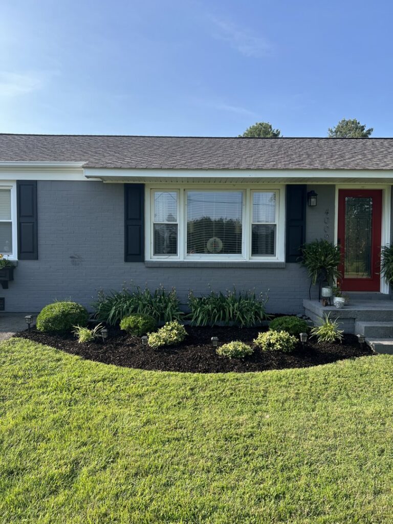 The front of a house showcasing newly installed mulched garden beds and fresh plantings by The Otherside Lawn Solutions in Ankeny, IA.