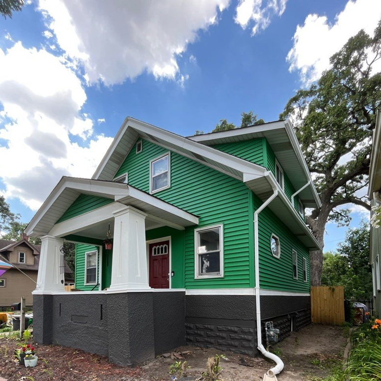 A residential house showcasing new green siding installed by Storm Group Roofing in Brooklyn Park, MN.