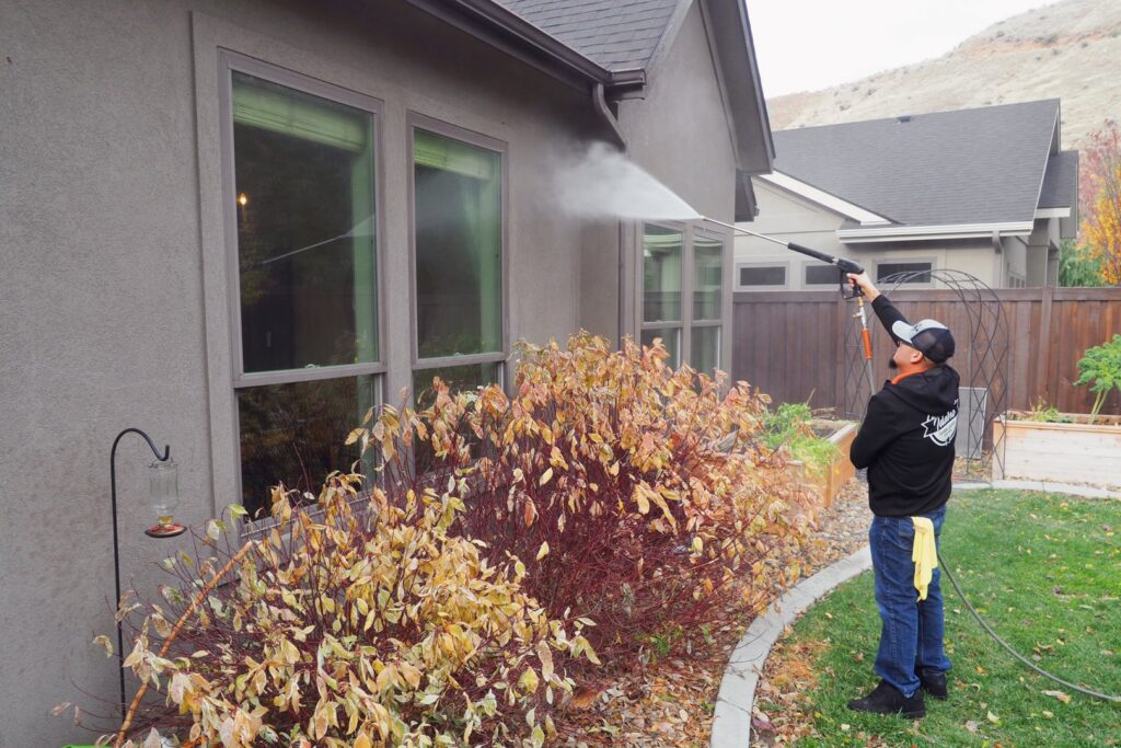 A house cleaner from Idaho Gem Cleaning performing pressure washing service on a house exterior in Caldwell, ID.