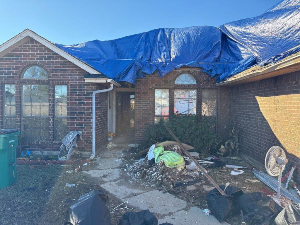 A house with a blue tarp covering the roof after storm or water damage, with cleanup by Service Professionals in Edmond, OK.
