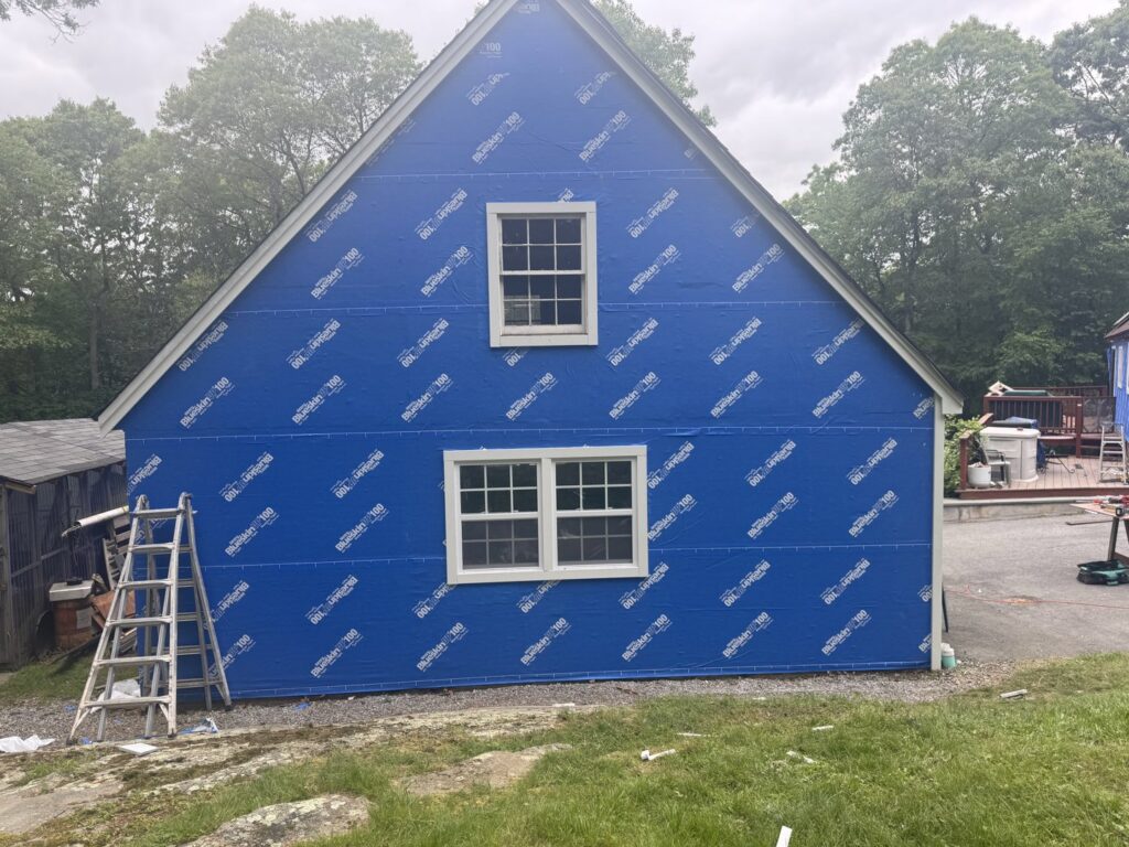 The side of a house wrapped in blue house wrap, ready for siding installation by J&J Rivera Roofing and Supply Co in Old Saybrook, CT