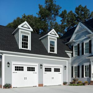 A beautiful house featuring two newly installed white garage doors with windows and decorative hardware by Overhead Door Company of Salt Lake in Sandy, UT.