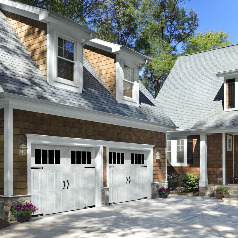 A residential property showcasing two white garage doors with windows and decorative hardware, expertly installed by Overhead Door Company of Salt Lake in Sandy, UT.