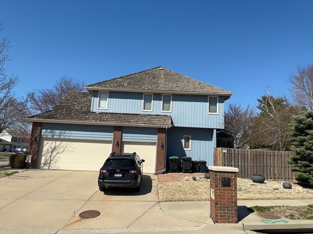 A residential home featuring blue siding and a distinctive wood shake roof, a project by Bishop Exteriors in Omaha, NE.