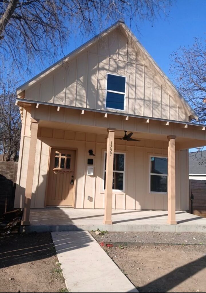 A charming house with tan board and batten siding and a wooden front door, a completed project by Ideal Siding Austin in Austin, TX.