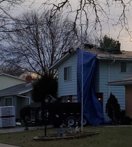 A house covered with a blue tarp after storm damage, indicating ongoing water damage repair by Barbera Home Improvement in Parma, OH.