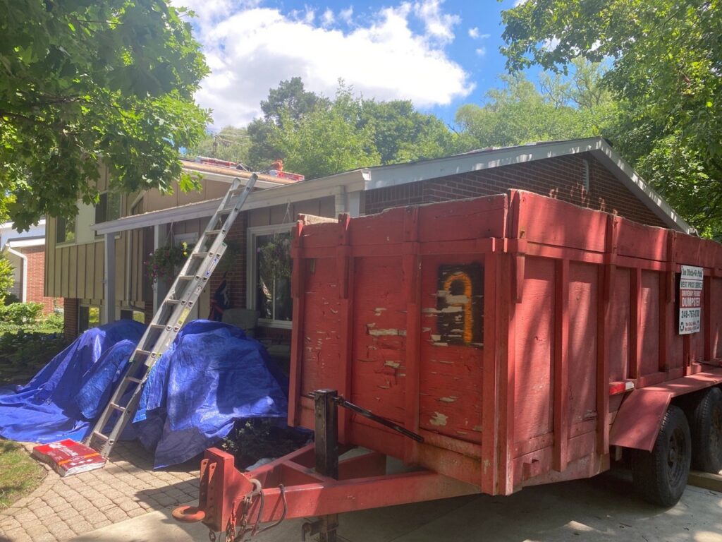 A house with blue tarps on the roof and a large dumpster for debris removal by Incore Restoration Group in Wixom, MI.