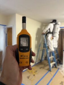 A humidity meter being used while a worker in a hazmat suit performs water damage or mold remediation for NSH Home Services in Jersey City, NJ.