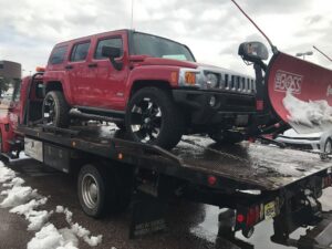 A red Hummer with a snowplow loaded onto a flatbed tow truck by Towing Colorado in Colorado Springs, CO.