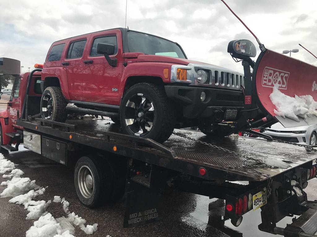A red Hummer with a snowplow loaded onto a flatbed tow truck by Towing Colorado in Colorado Springs, CO.