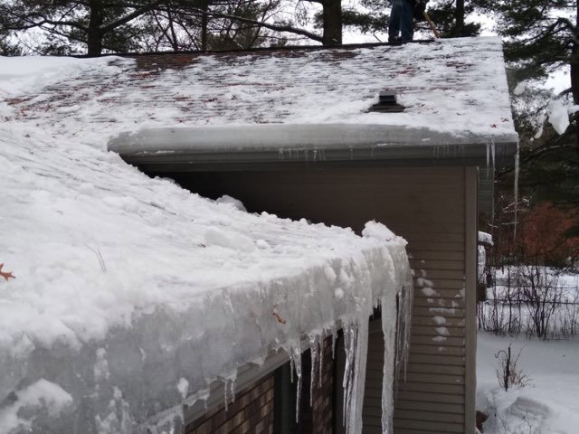 A roof covered in snow and large icicles, indicating ice damming, a common cause of water damage, addressed by Local Clean Up Specialists in Green Bay, WI.