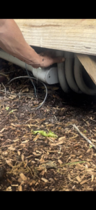 A hand pointing to a leaking pipe under a structure, indicating a water damage issue at South Shore Leak Solutions in Quincy, MA