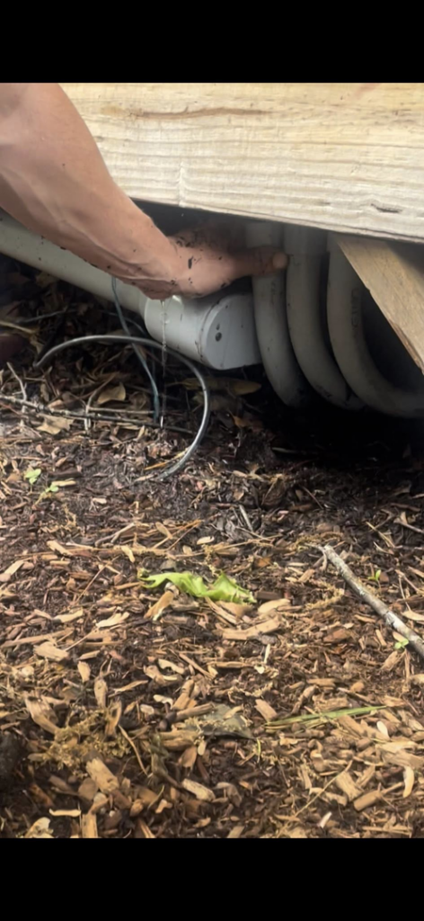 A hand pointing to a leaking pipe under a structure, indicating a water damage issue at South Shore Leak Solutions in Quincy, MA