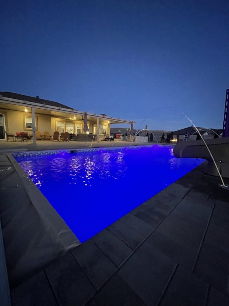 An illuminated pool with blue lighting and elegant water features at dusk, showcasing a project by Battle Born Pool & Spa in Sparks, NV.
