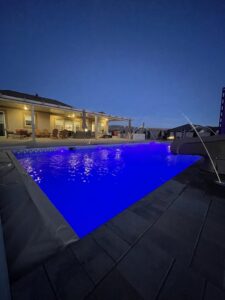 An illuminated swimming pool at night with vibrant blue lights and water features, by Battle Born Pool & Spa in Sparks, NV.