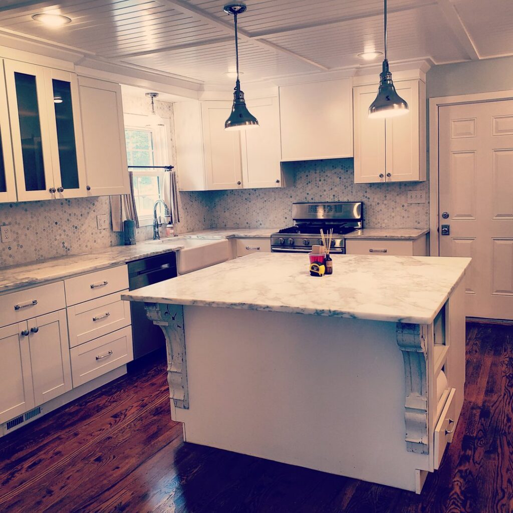 An immaculate kitchen featuring white cabinets, a marble island, and dark hardwood floors, cleaned by A To Zen in Lansing, MI.
