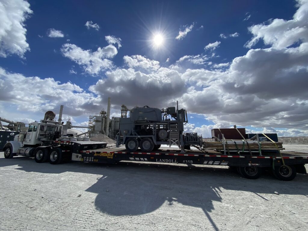 Affordable Towing LLC transporting industrial equipment and lumber on a flatbed trailer under a sunny sky in Anaheim, CA.