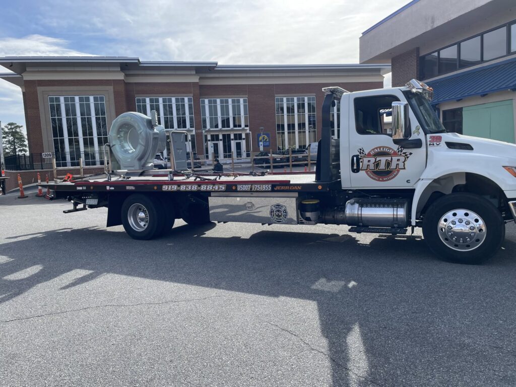 A flatbed tow truck from Raleigh Towing & Recovery transporting industrial equipment in Raleigh, NC.