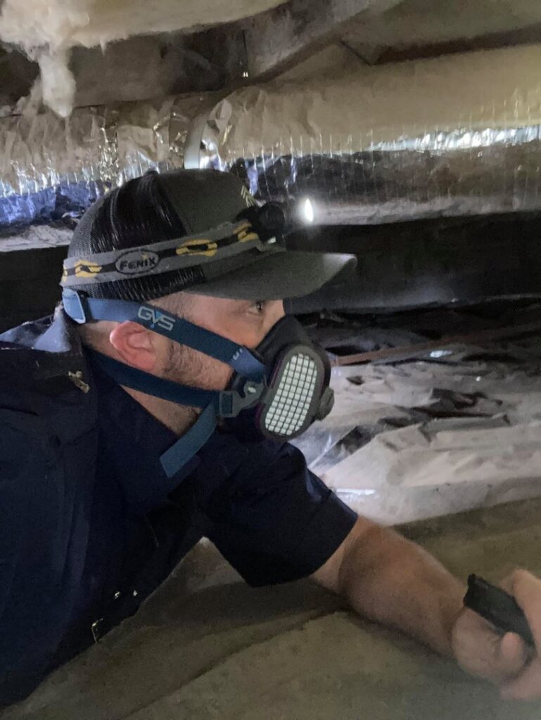 A Double H Inspections specialist wearing a respirator and headlamp while inspecting a tight crawlspace in Sheridan, WY