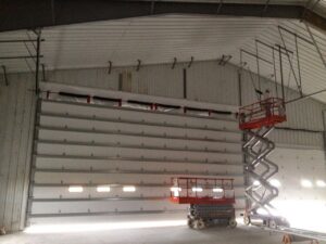 Interior view of a large commercial garage door installation with a scissor lift and visible tracks by Alberts Custom Door Company in Wichita, KS.