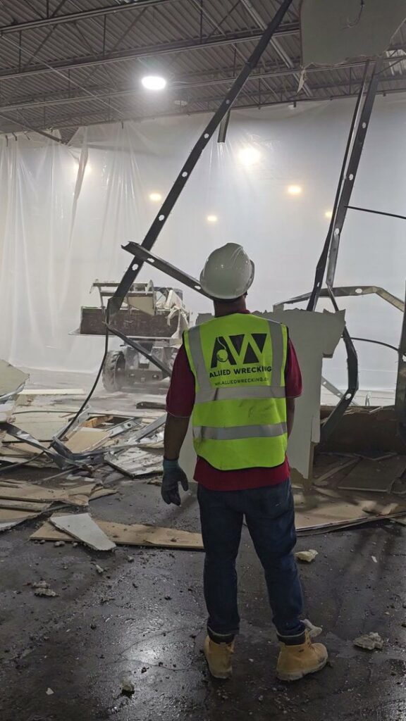 A worker overseeing interior demolition with a skid steer in the background for Allied Wrecking Boston in East Boston, MA.