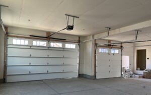 Interior view of a residential garage with two white garage doors and openers installed by Barrett Overhead Doors in Idaho Falls, ID.