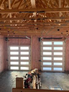 Interior view of two modern white garage doors with horizontal windows installed in a framed garage by Devildog Dock N Door in Helena, MT.