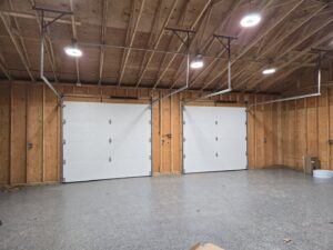 Interior view of a garage with two newly installed white garage doors and openers by Spring King Garage Doors in Middletown, CT