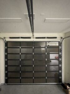 Interior view of a modern dark glass panel garage door with tracks and springs, installed by NV Pro Garage Doors in Las Vegas, NV.