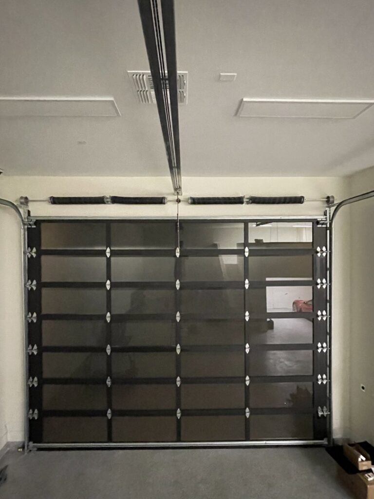 Interior view of a modern dark glass panel garage door with tracks and springs, installed by NV Pro Garage Doors in Las Vegas, NV.