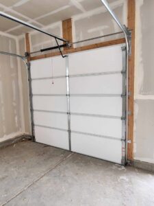 An interior view of a white garage door installation with tracks and springs by Layton Doors in West Jordan, UT.