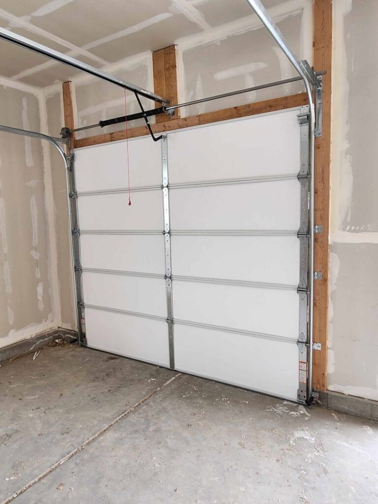 An interior view of a white garage door installation with tracks and springs by Layton Doors in West Jordan, UT.