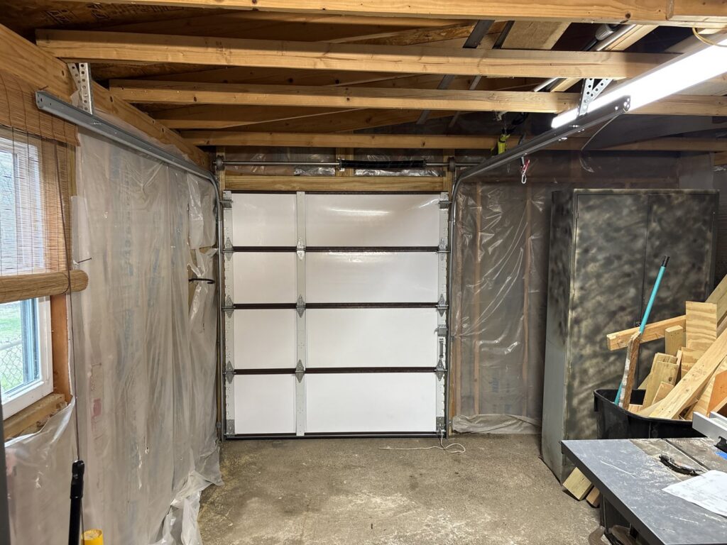 Interior view of a garage showing a newly installed white sectional garage door and tracks by GRIT Garage Doors in Alma, AR