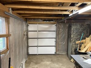 Interior view of a garage showing a newly installed white sectional garage door and tracks by GRIT Garage Doors in Alma, AR