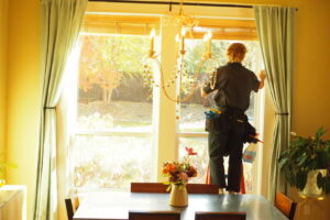 A professional cleaning an interior window while standing on a ladder by Idaho Gem Cleaning in Caldwell, ID.