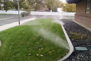 An irrigation system watering a strip of green grass next to a commercial building, provided by Love it Lawn Care in Butte, MT