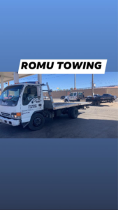 An Isuzu flatbed tow truck from ROMU Towing in El Paso, TX, parked on the side of a road.