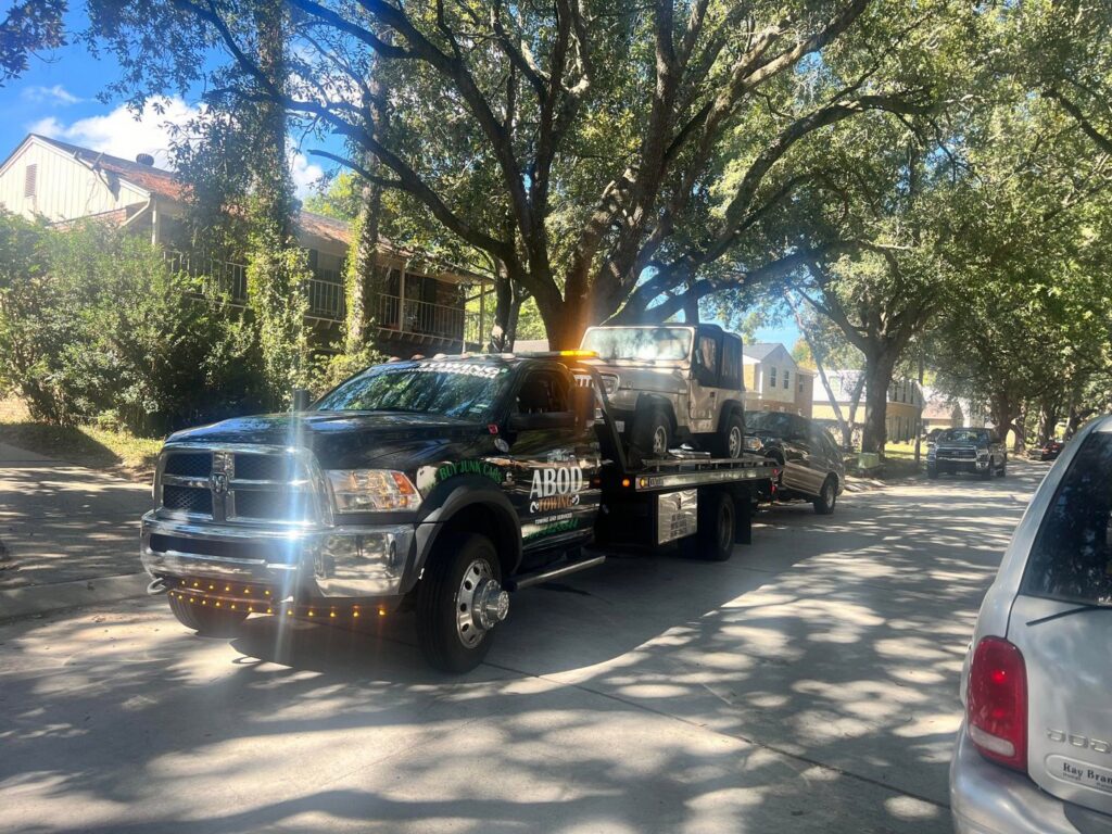 A white Jeep and another car being towed by a flatbed tow truck from ABOD Towing LLC in New Orleans, LA.