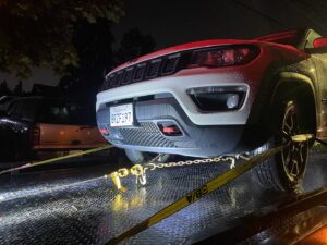 A white Jeep Compass securely loaded on a flatbed tow truck from Safety AUTO Towing LLC in Seattle, WA, at night.