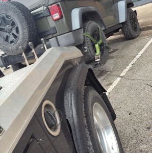 The rear wheel of a Jeep secured with straps on a tow truck from Towing Near Me 247 LLC Dallas in Dallas, TX.