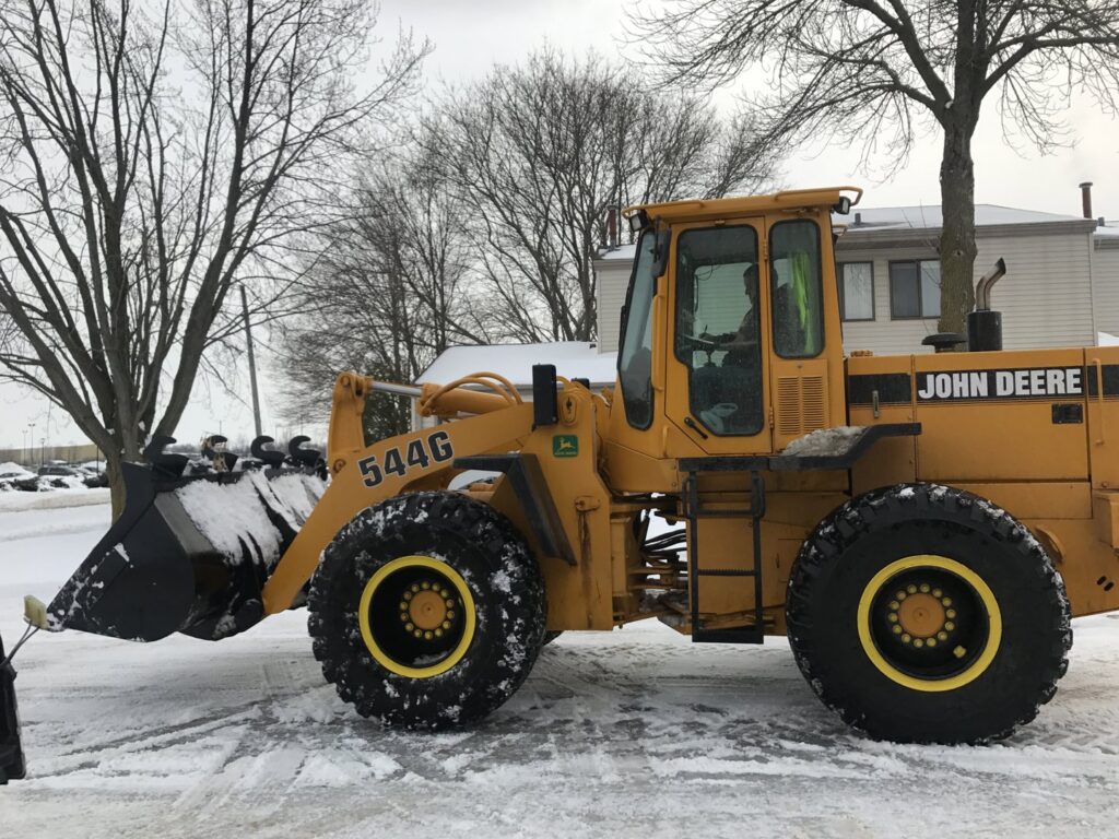 A yellow John Deere front-end loader equipped with a snow plow, ready for snow removal services by Appleton Snow Removal in Appleton, WI.