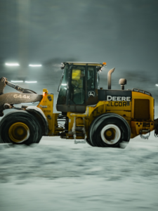 A yellow John Deere loader with the Elcor Construction logo moving snow in Rochester, MN.