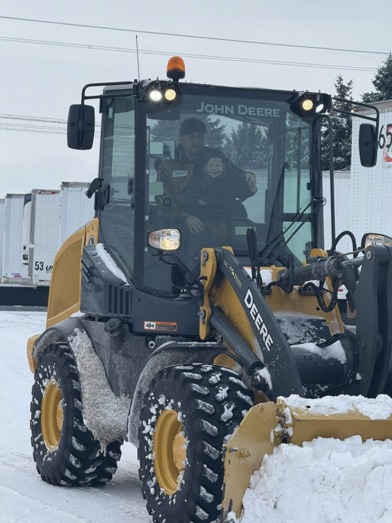 A John Deere loader with a plow attachment actively clearing snow for Cities Lawn and Snow LLC in Woodbury, MN.