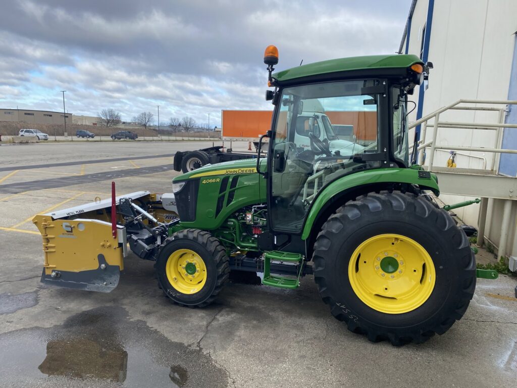 A green John Deere tractor equipped with a yellow snow plow, ready for snow removal by Turf Pro Lawn Care & Snow Removal in Green Bay, WI.