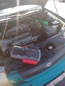 A portable jump starter device placed on the engine of a green car with the hood open, ready to provide a jump start service by Emergency Towing Sacramento, CA.