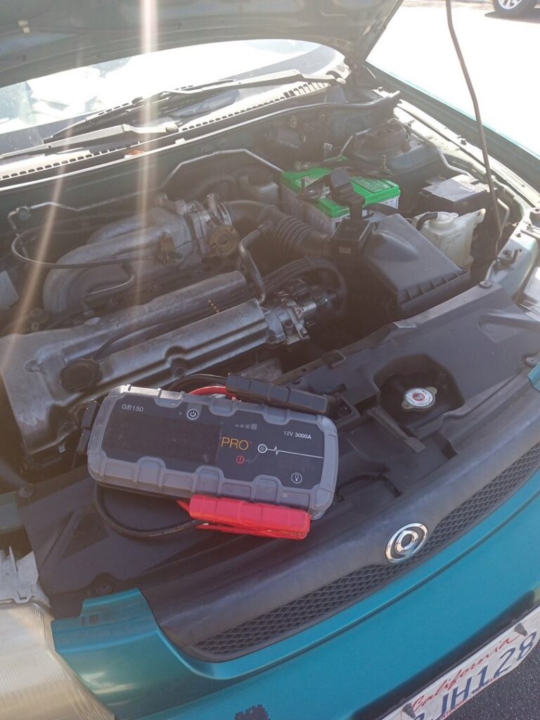 A portable jump starter device placed on the engine of a green car with the hood open, ready to provide a jump start service by Emergency Towing Sacramento, CA.