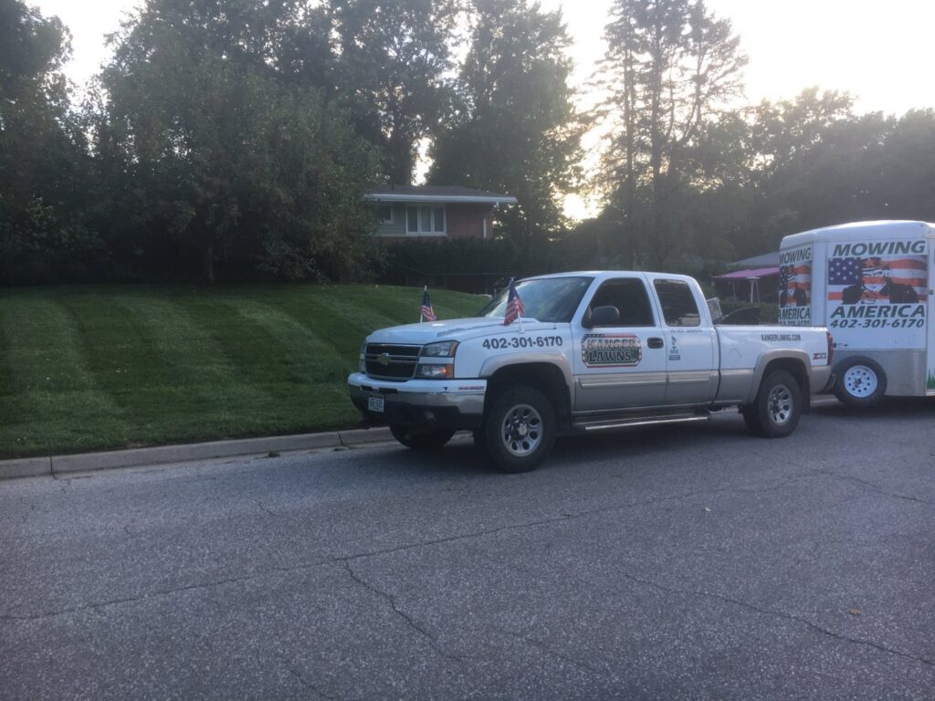 A Kanger Lawns LLC truck and trailer parked next to a freshly mowed lawn with distinct stripes in Omaha, NE.