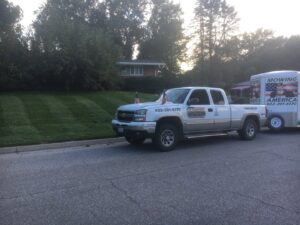 A Kanger Lawns LLC truck and trailer parked next to a freshly mowed lawn with distinct stripes in Omaha, NE.