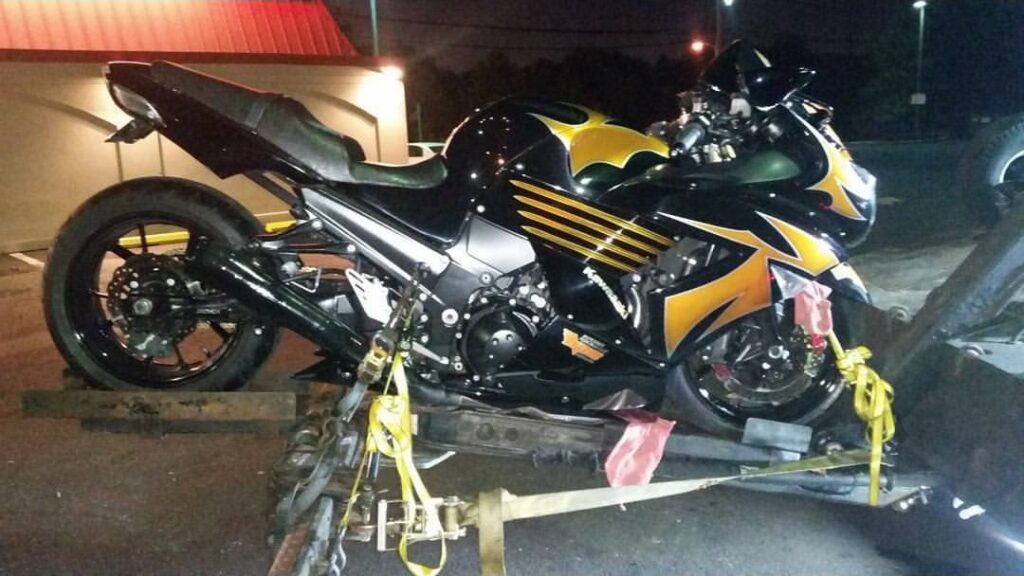 A black and yellow Kawasaki motorcycle being loaded onto a tow truck by Whitelock Towing in Baltimore, MD, at night.