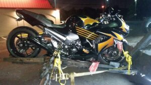A black and yellow Kawasaki motorcycle being loaded onto a tow truck by Whitelock Towing in Baltimore, MD, at night.